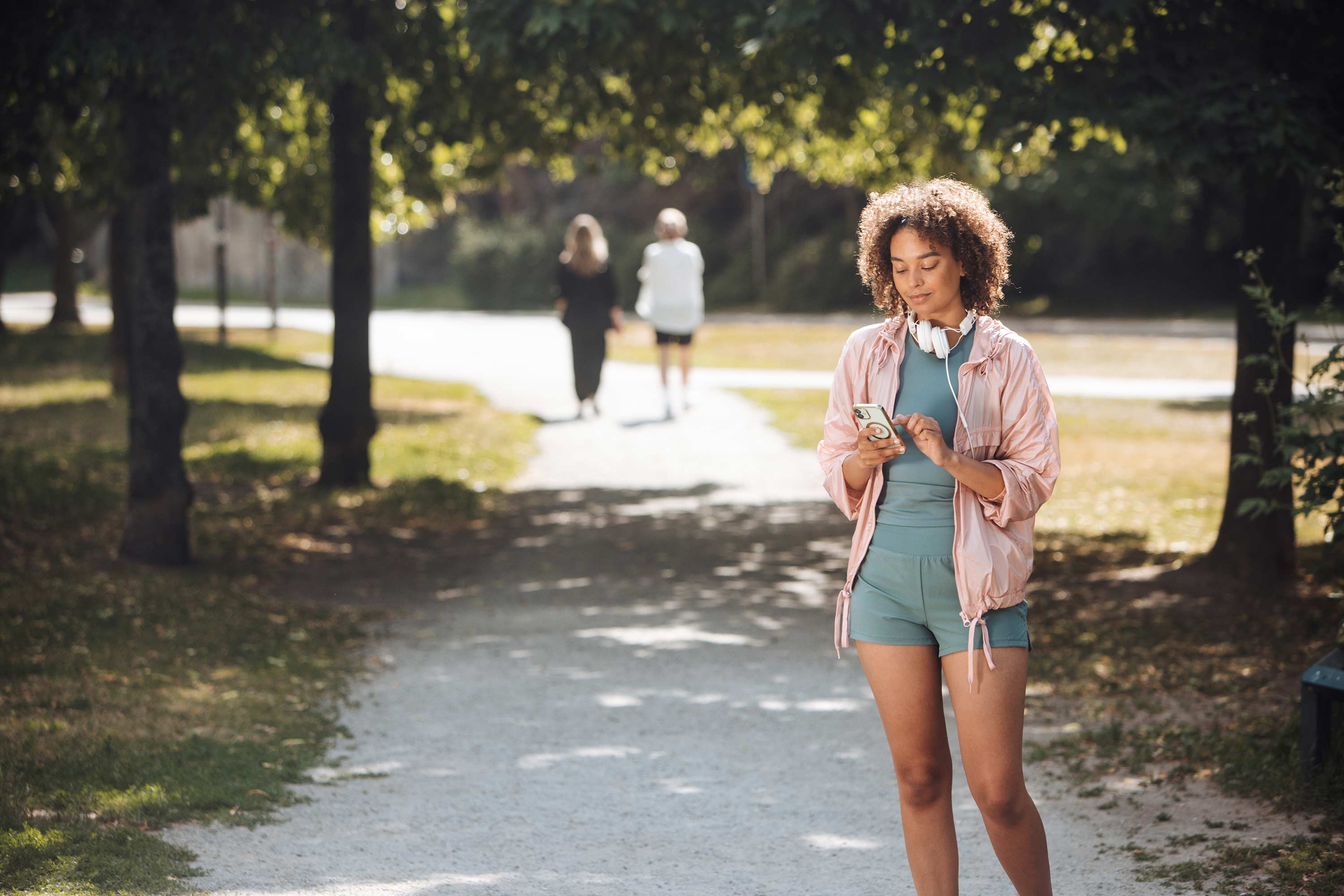 Tjej iklädd träningskläder står i en park och tittar på sin mobiltelefon
