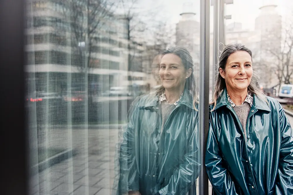 En kvinnlig teknisk förvaltare står lutad mot en fastighet och ler mot kameran.