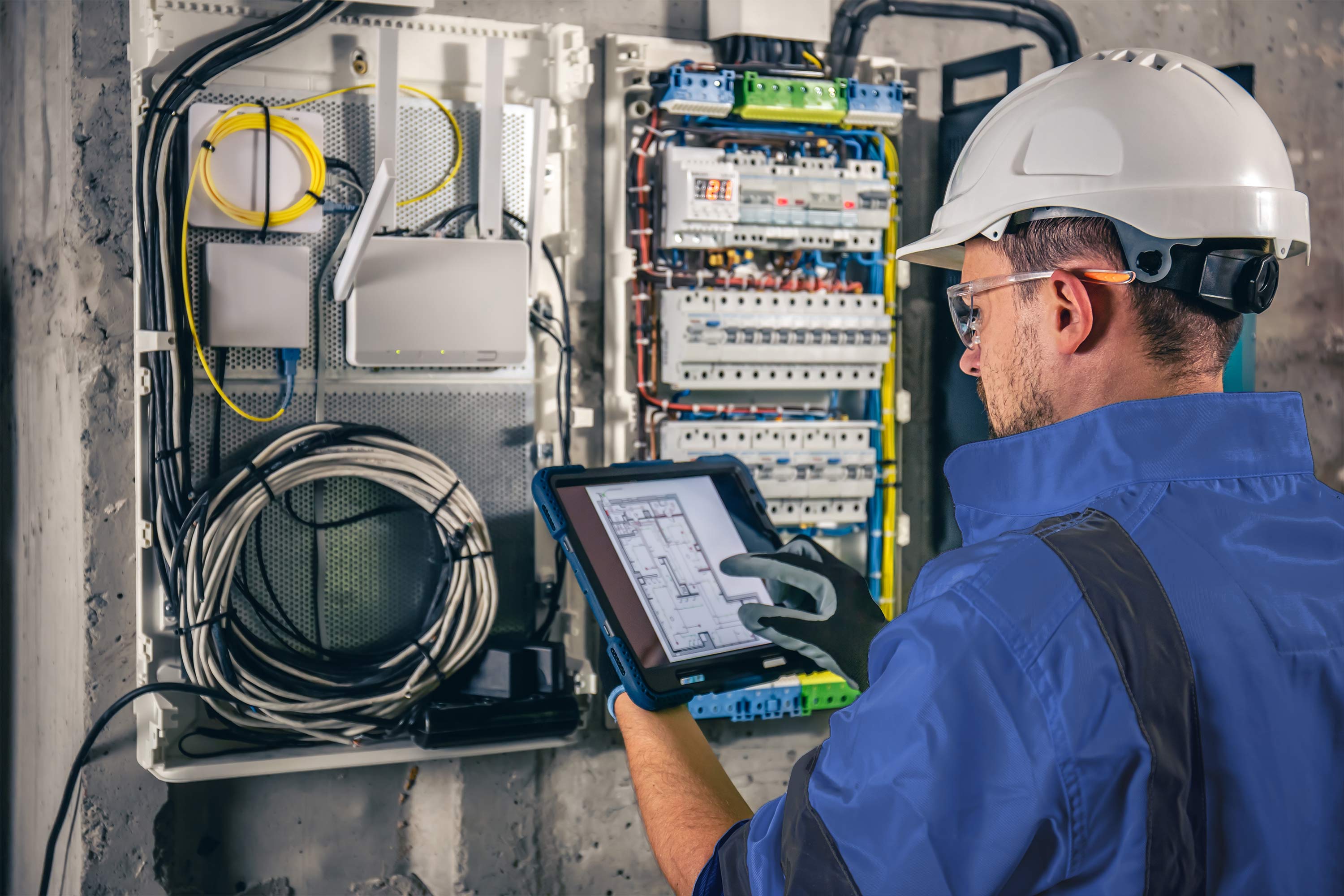 man i blå skjorta med hjälm kontrollerar elanläggningen i ett elskåp