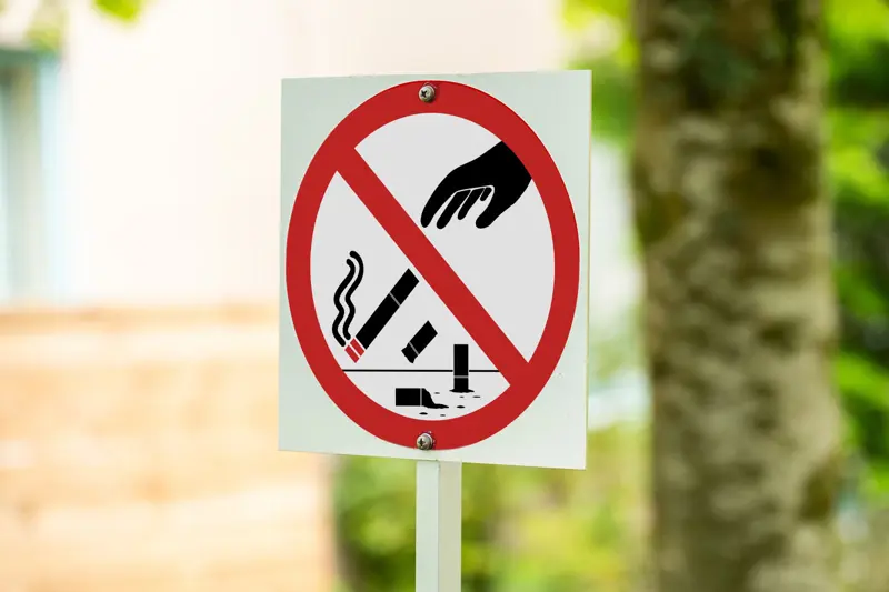 Skylt med ett rött streck över en hand som kastar cigarettfimpar.