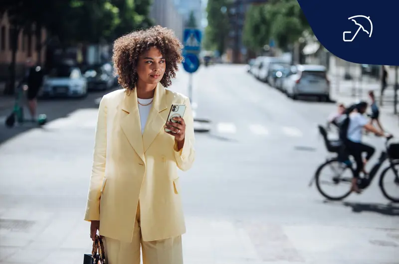 Kvinna i gul kostym står på gatan med mobiltelefon i handen.