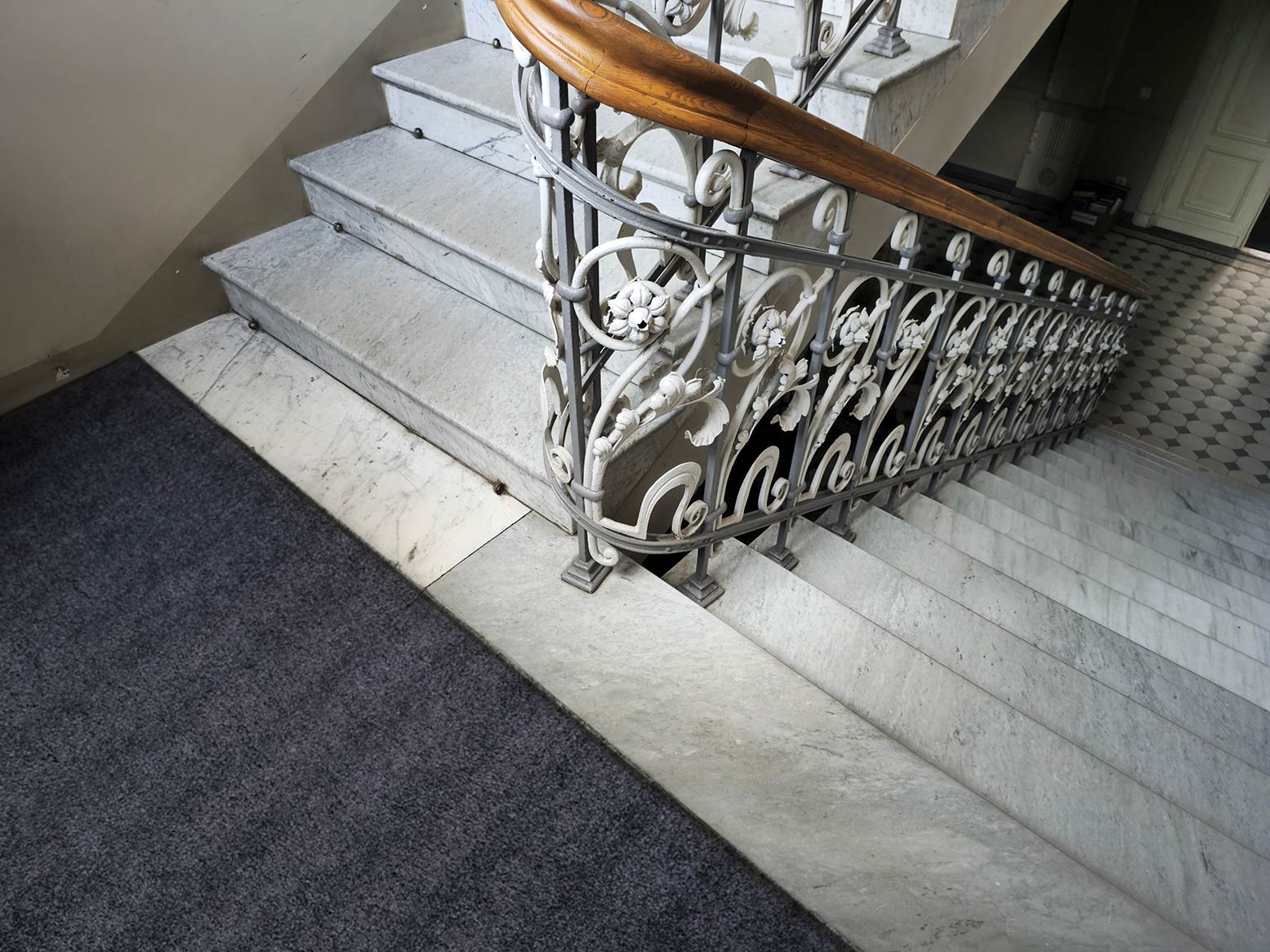 Marmortrappa i ett trapphus i en bostadsrättsförening, sett ovanifrån. Med en mörkgrå entrématta på golvet.