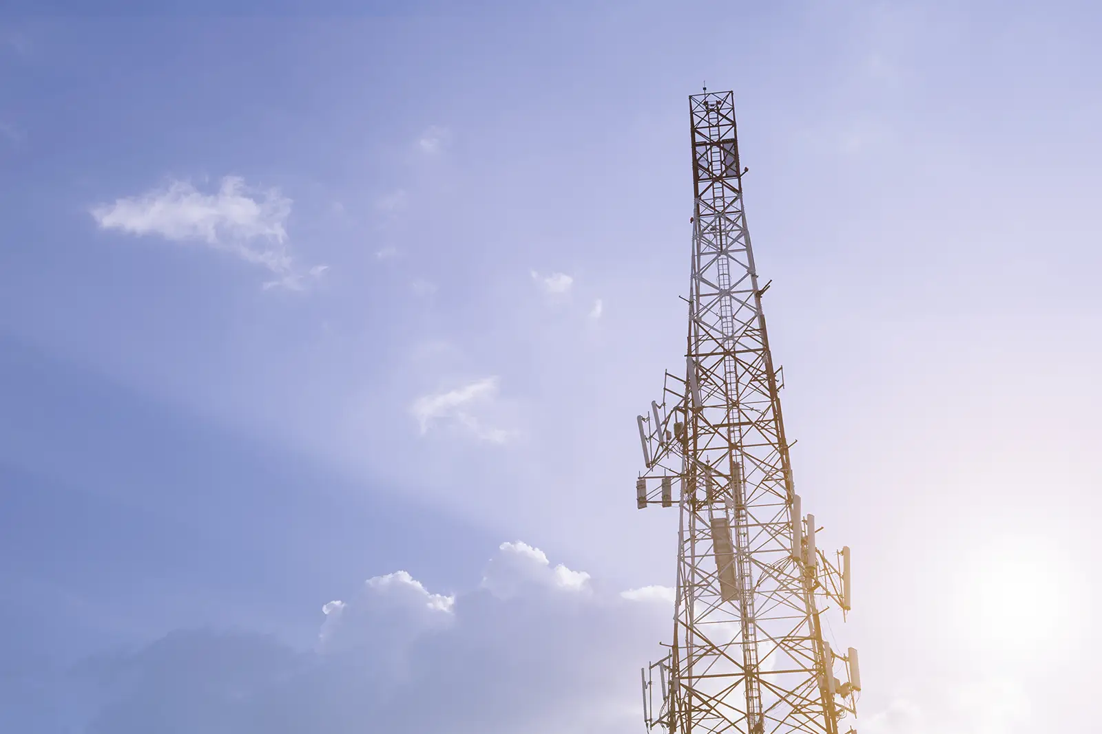 Telekommunikationstorn mot blå himlen med moln.